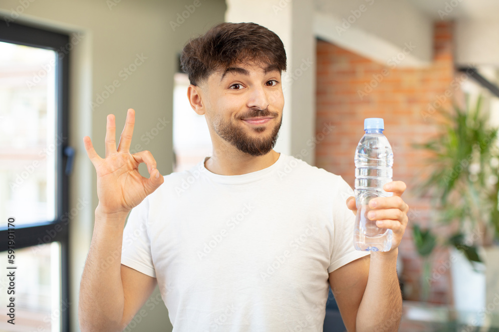young handsome man feeling happy, showing approval with okay gesture. water bottle concept young handsome man feeling happy, showing approval with okay gesture. water bottle concept