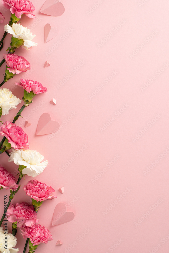 Mother's Day concept. Top vertical view flat lay of delightful carnation flowers, and pink paper hearts on a soft pastel pink background with copyspace