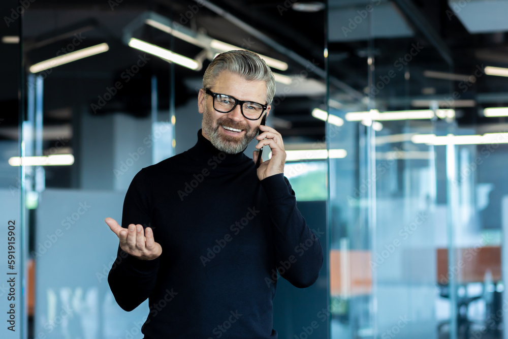 Φωτογραφία Portrait of an older gray-haired businessman standing in the office and smiling talking on the phone