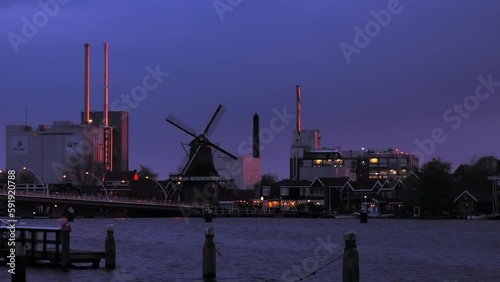 Zaanse Schans, Netherlands - April 25, 2022: Blue hour - dusk - in industrial zone of Zaanse Schans with factories and a spinning windmill.