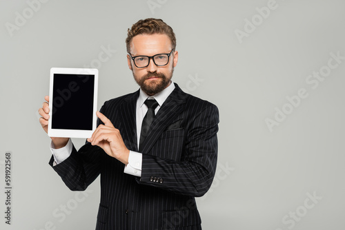 bearded businessman in formal wear and glasses holding digital tablet with blank screen isolated on grey.