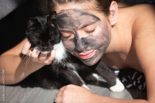Morning with black cat. Woman with charcoal facial mud mask on face. Cosmetic procedure. Beauty spa and cosmetology. Spa woman applying gray facial clay mask. Beauty treatments.