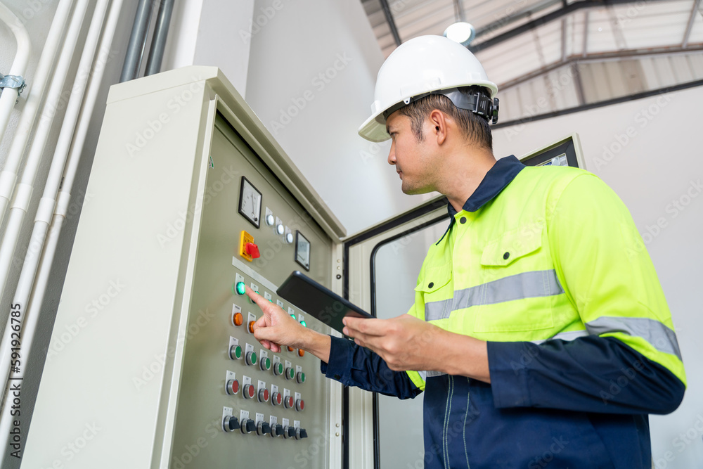 Asian engineer or electrician working on electrical check of water supply system control cabinet with tablet at factory Asian engineer or electrician working on electrical check of water supply system control cabinet with tablet at factory