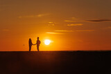 silhouette of couple at sunset, woman and man holding hands walking along seashore in rays of sunset sunlight. walk and hug. place for text, romantic relationships, freedom and carelessness