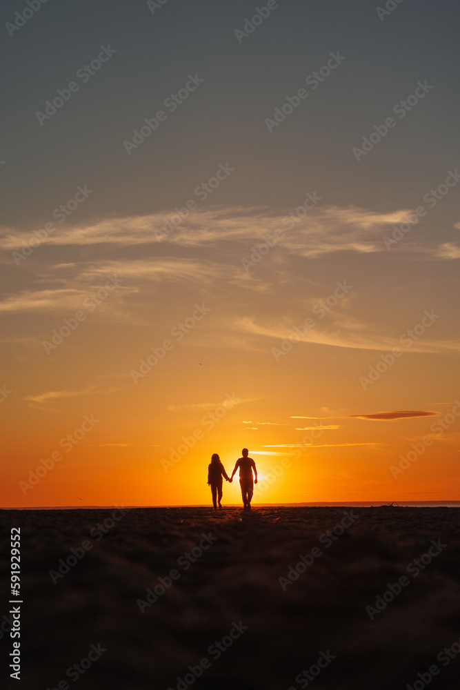 silhouette of a couple at sunset, woman and man walking along seashore in rays of sunset sunlight. walk and hug. place for text, romantic relationships, freedom and carelessness