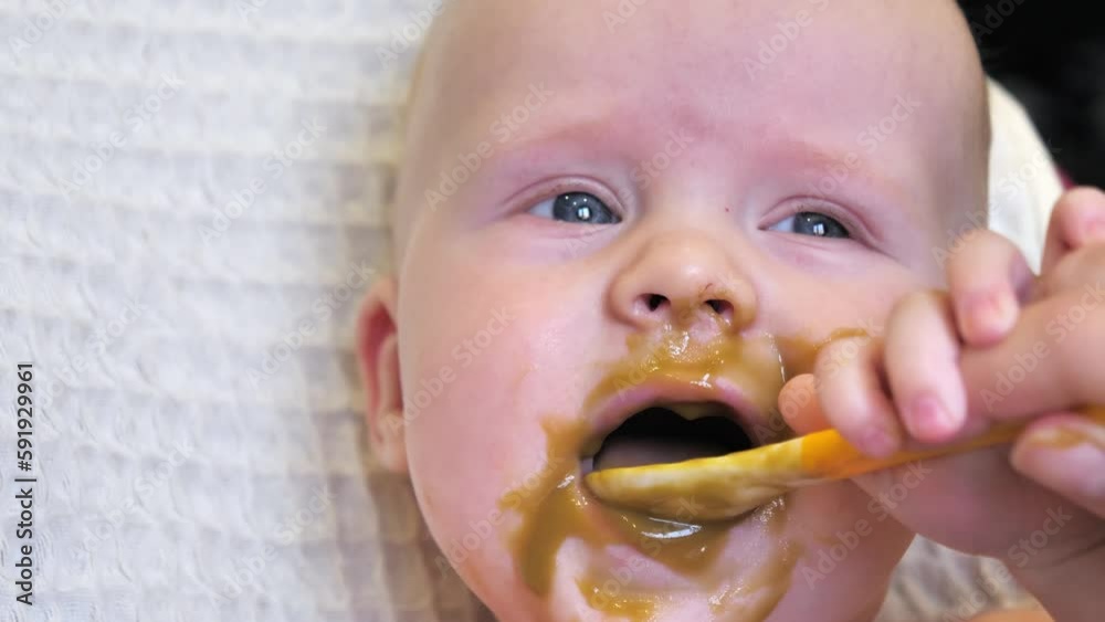 Mom feeding little boy with broccoli puree. Child at the age of six months eats broccoli while sitting on a baby chair. Slow motion shot. Mom feeding little boy with broccoli puree. Child at the age of six months eats broccoli while sitting on a baby chair. Slow motion shot.