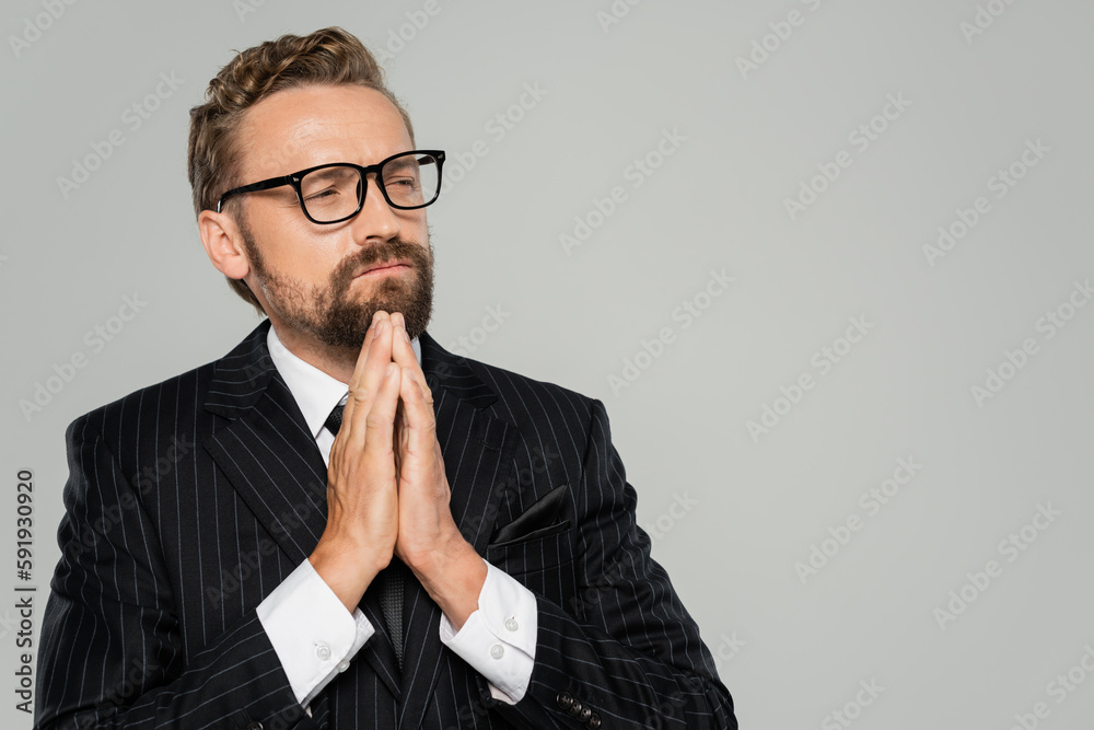 thoughtful businessman in formal wear and glasses standing with folded hands isolated on grey. thoughtful businessman in formal wear and glasses standing with folded hands isolated on grey.