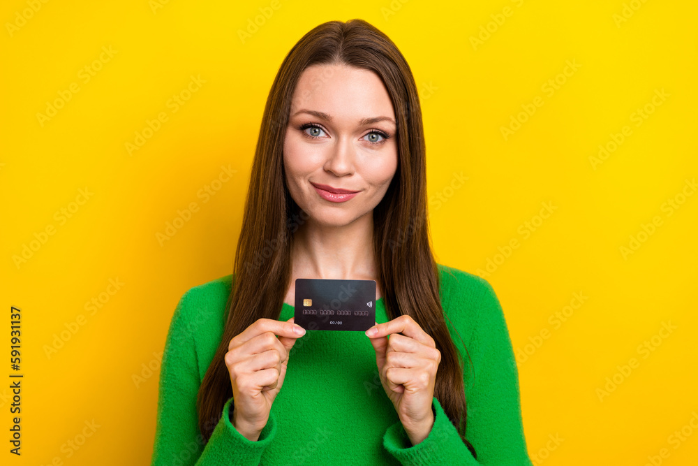 Photo of pretty friendly girl hands hold demonstrate plastic debit card isolated on yellow color background Photo of pretty friendly girl hands hold demonstrate plastic debit card isolated on yellow color background