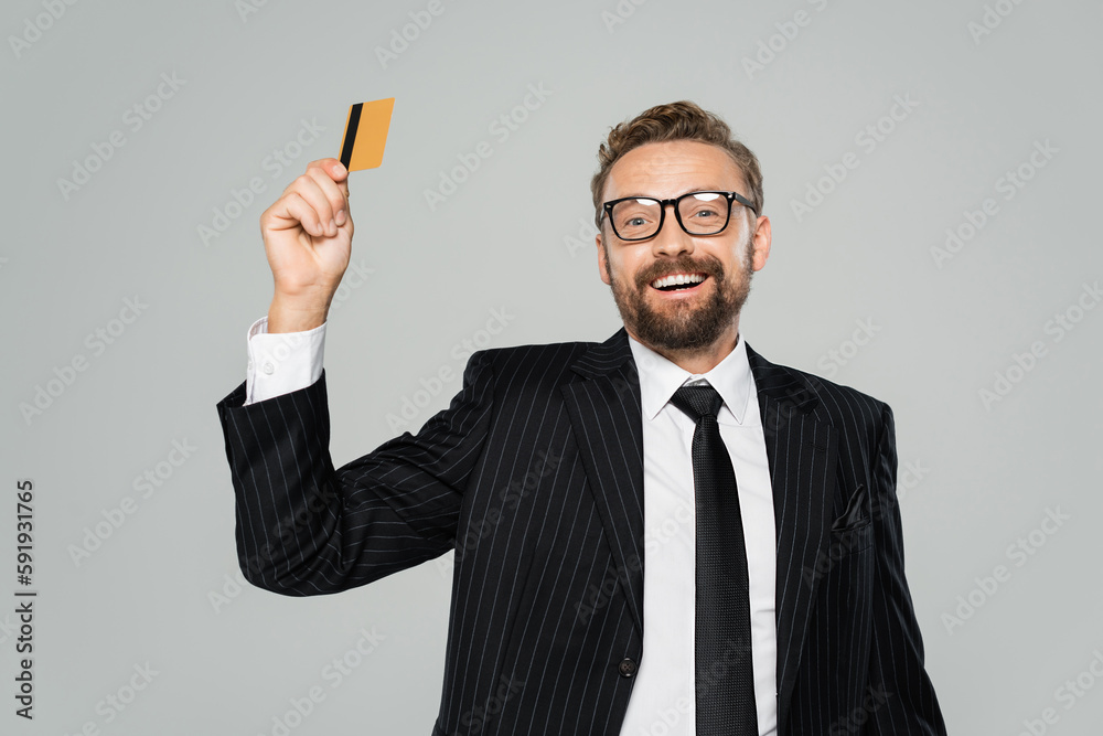 positive businessman in suit and glasses holding credit card isolated on grey. positive businessman in suit and glasses holding credit card isolated on grey.