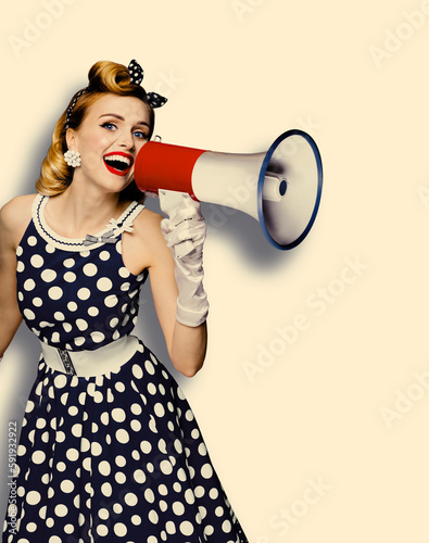 Portrait image of beautiful woman holding mega phone, shout, saying, advertising. Pretty girl in black pin up dress with megaphone loudspeaker. Isolated against background. Big sales ad. Vintage.