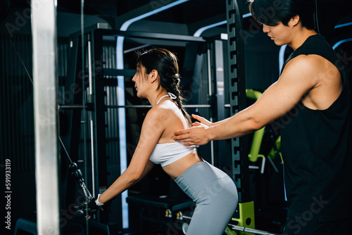 Smiling coach instructing a woman on how to use a pull-down weight machine, focusing on building muscular strength and endurance. GYM healthy lifestyle concept