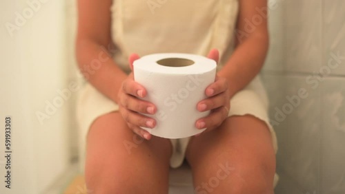 woman sitting on the toilet playing with toilet paper photo