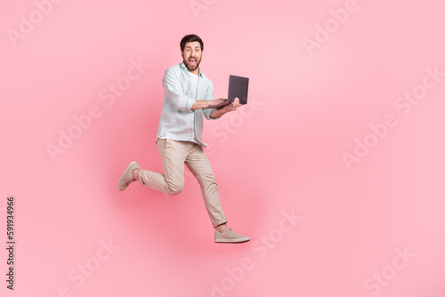 Full length photo of cheerful excited man wear turquoise shirt chatting modern gadget empty space isolated pink color background