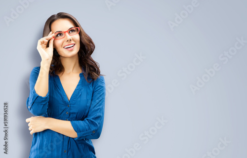 Portrait of happy smiling brunette woman looking up, in red eye glasses, blue confident wear, isolated grey gray background. Business studio concept. Copy space area for text.