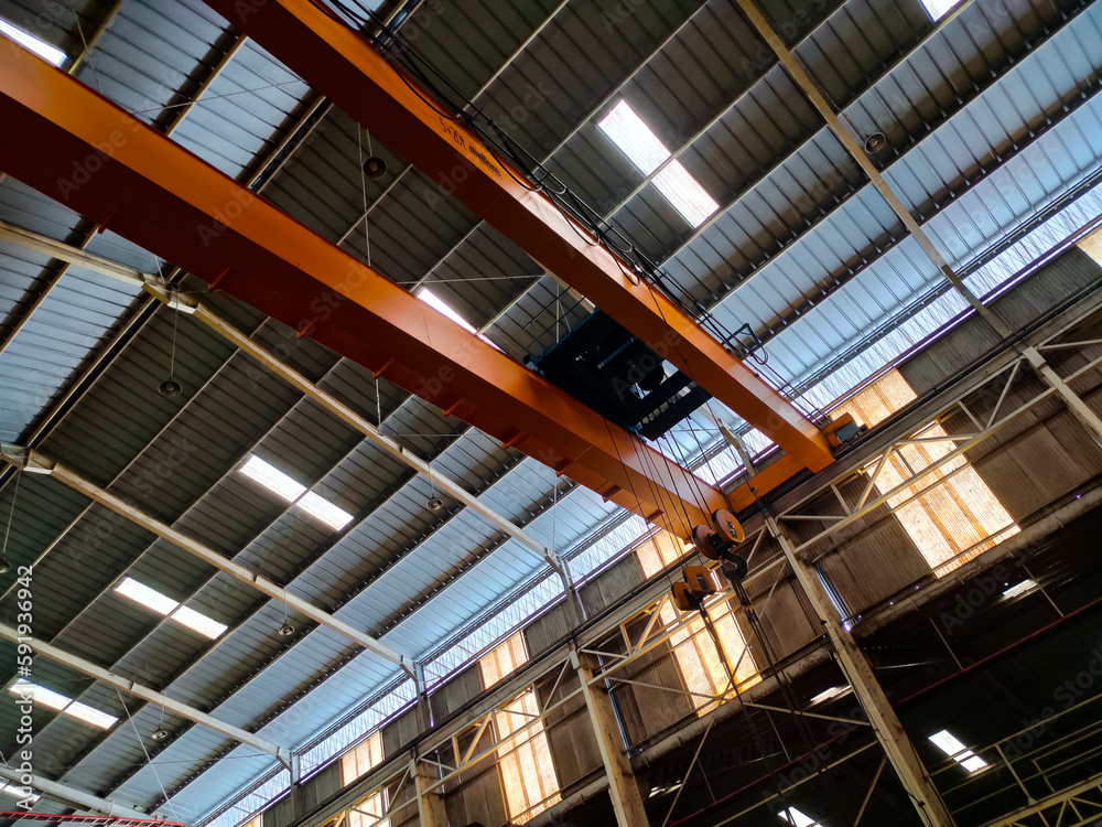 Yellow overhead crane installed on the manufacturing industry plant shop. Jib crab trolley with hooks and linear traverse.

