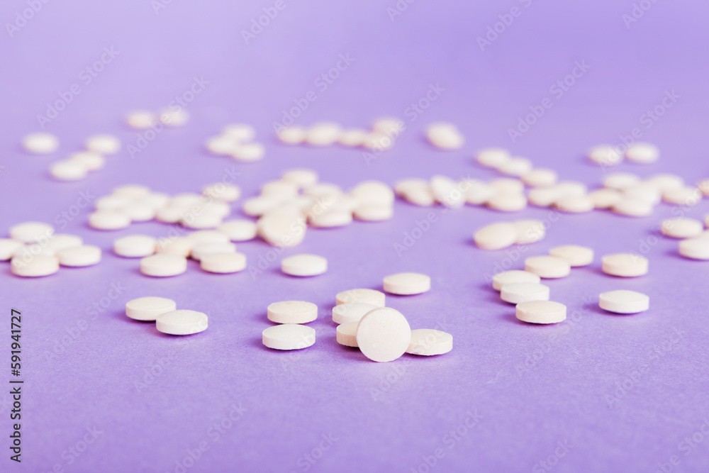 Heap of white pills on colored background. Tablets scattered on a table. Pile of red soft gelatin capsule. Vitamins and dietary supplements concept Heap of white pills on colored background. Tablets scattered on a table. Pile of red soft gelatin capsule. Vitamins and dietary supplements concept