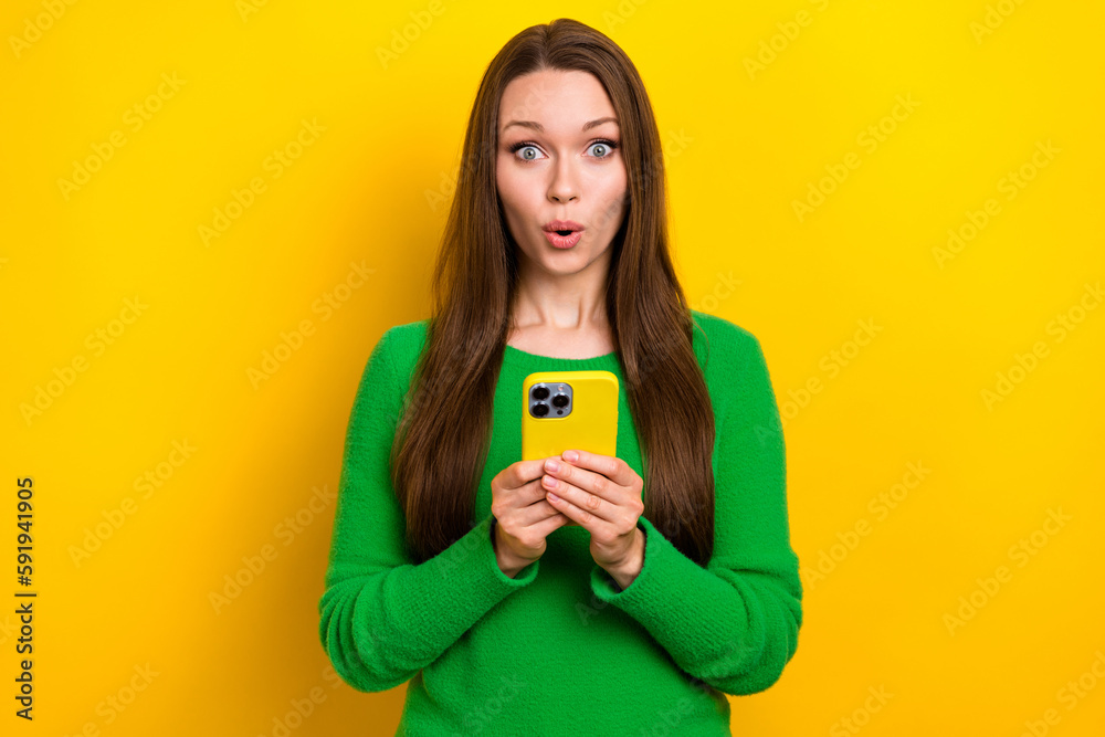 Portrait of astonished pretty girl hold use smart phone pouted lips isolated on yellow color background