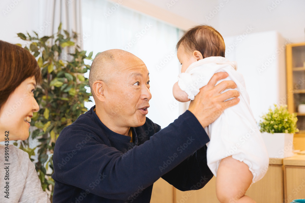 Fototapeta premium 自宅で孫の赤ちゃんを抱っこする祖父とそれを見守る祖母の3人