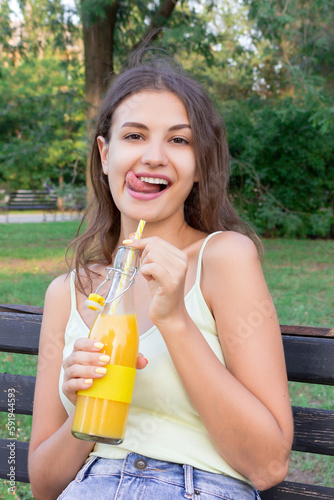 Cute girl is relaxing in the park and drinking cool juice in a hot day