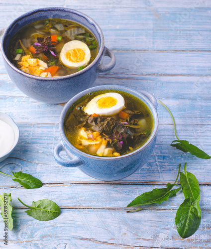 Rustic homemade soup with sorrel and egg, forest greens in spring recipes, rustic blue background. Light, dietary springtime soups photo