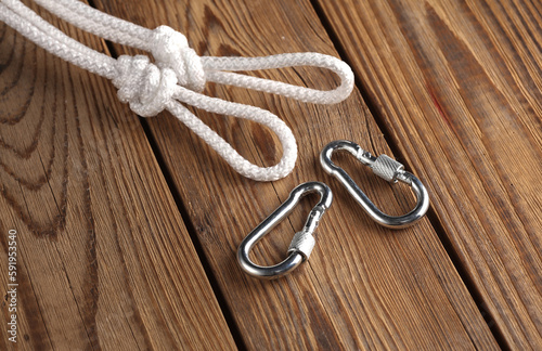 Rope with knots, loops and carabiners on wooden background. Safety rope, climbing equipment
