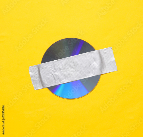 Cd disk fixed with adhesive tape on yellow background. Conceptual pop, contemporary art