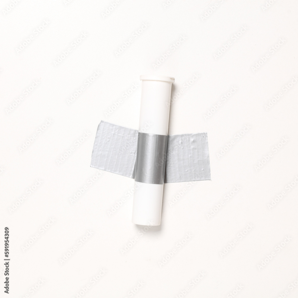 Obraz premium Pills tube fixed with adhesive tape on white background. Conceptual pop, contemporary art, minimalist still life