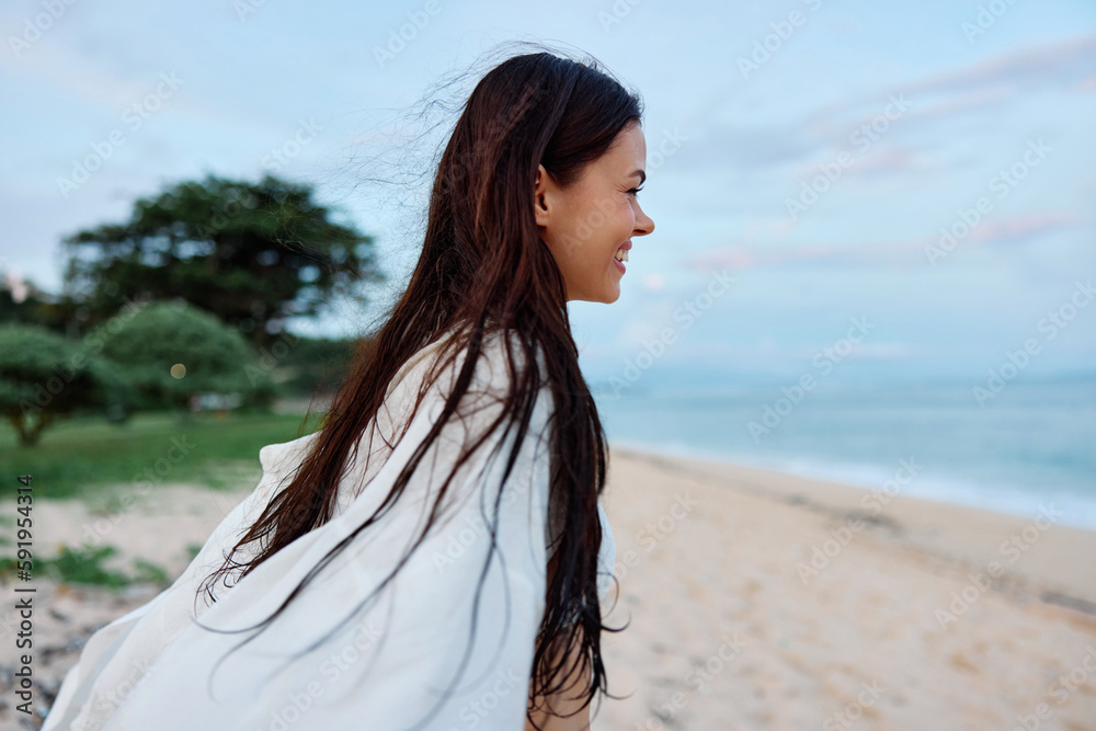 Brunette woman with long hair in a white shirt and jean shorts tan body abs and happiness fun smile with teeth on the beach and palm trees, vacation summer trip sunset sky