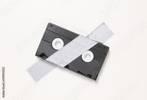 Video cassette fixed with adhesive tape on white background. Conceptual pop, contemporary art, minimalist still life