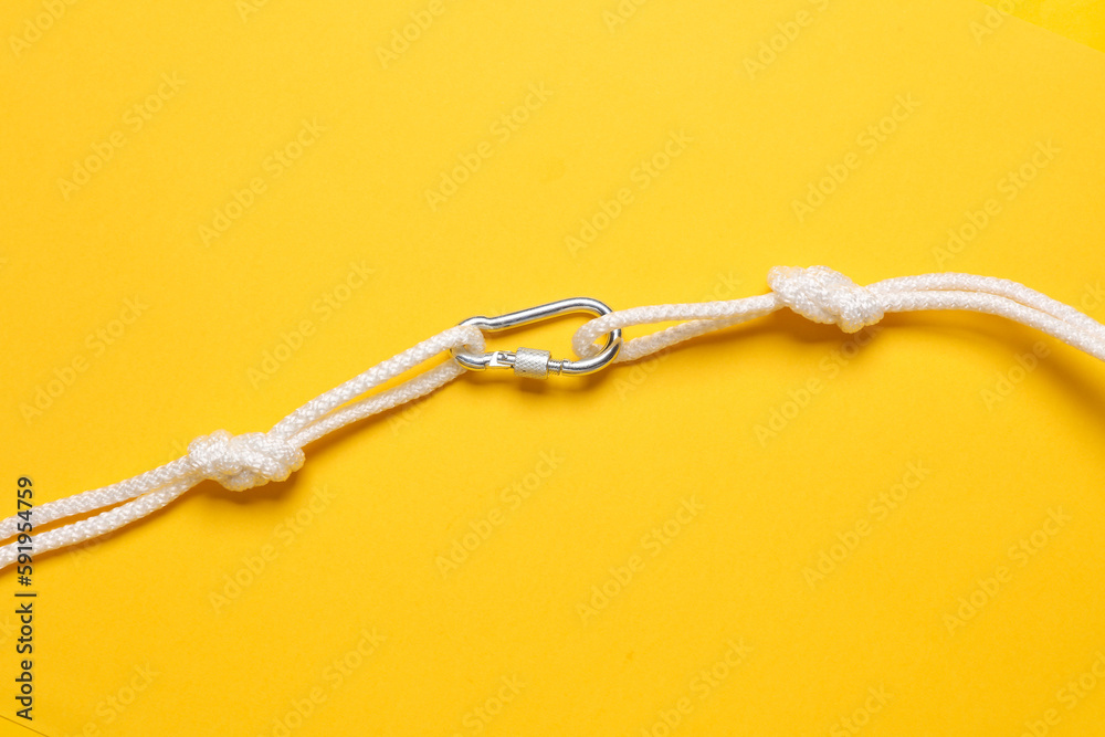 Rope with knots and carabiner on yellow background. Safety, climbing equipment