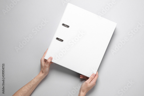 Fotografie Female hands holding a white binder folder on a gray background