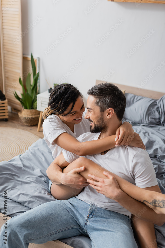 joyful african american woman embracing happy bearded boyfriend while having fun on bed at home. joyful african american woman embracing happy bearded boyfriend while having fun on bed at home.