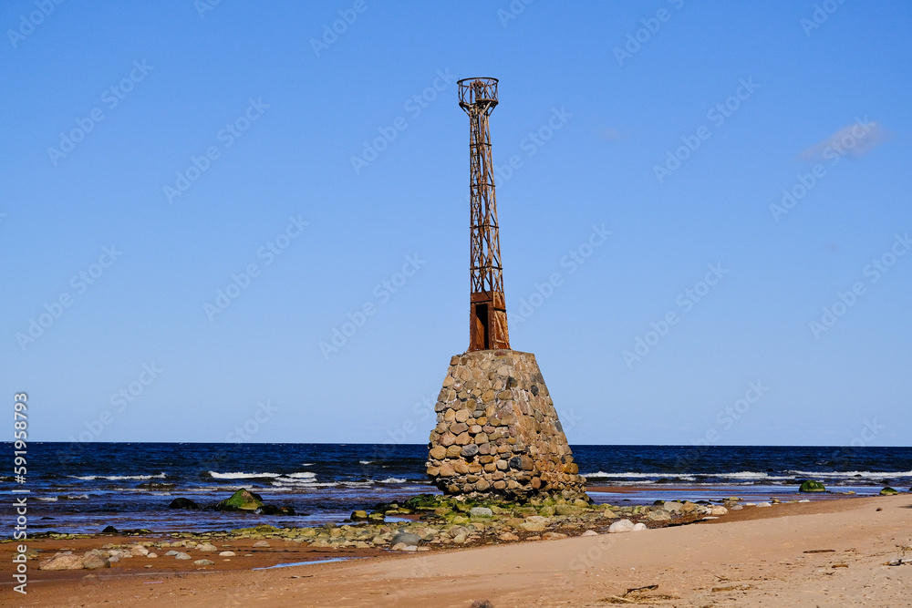 Fototapeta premium Ruins of the ancient Kurmrags lighthouse on the shore of the Gulf of Riga. Stone masonry in the lower part of the lighthouse, above which is the metal body of the lighthouse made in Sweden. Baltic Sea