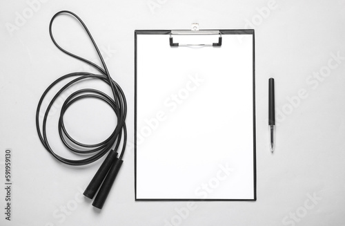 Workout plan, bodybuilding and fitness, weight loss. Clipboard with jump rope on gray background. Flat lay. Top view