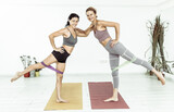 Two fitness women work out together with fitness rubber bands indoors. Healthy lifestyle, fitness concept