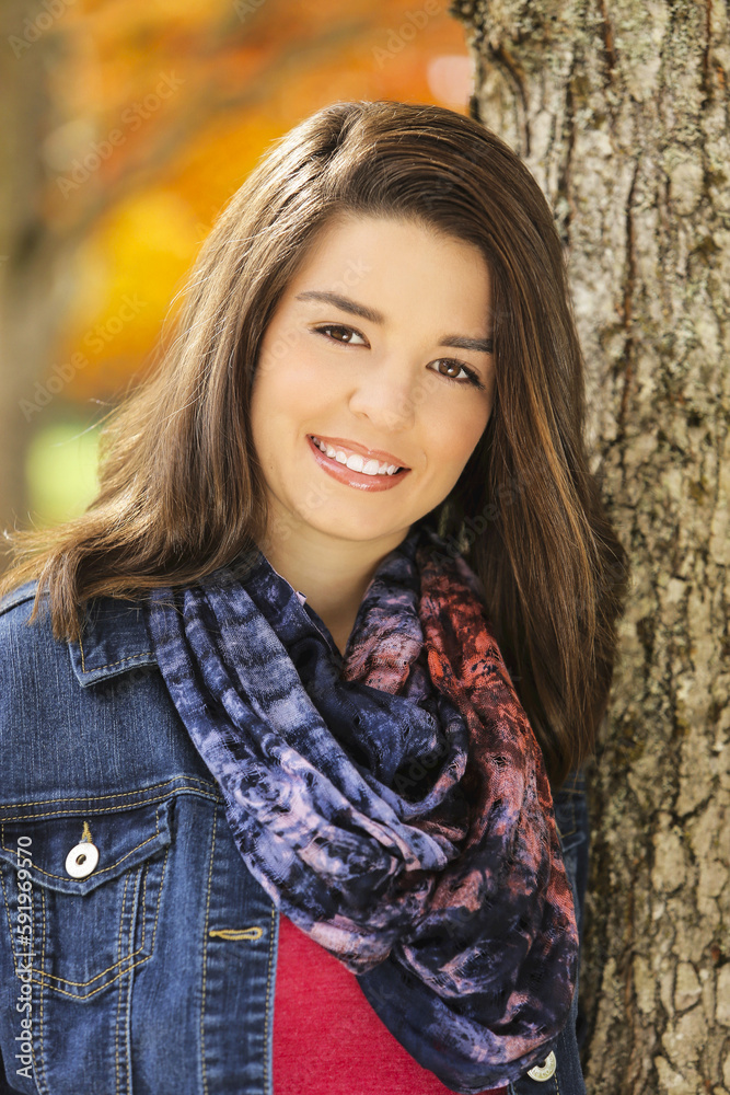 Portrait Of A Young Woman Standing Against A Tree Trunk With Autumn Colours In The Background; Oregon, United States Of America Portrait Of A Young Woman Standing Against A Tree Trunk With Autumn Colours In The Background; Oregon, United States Of America