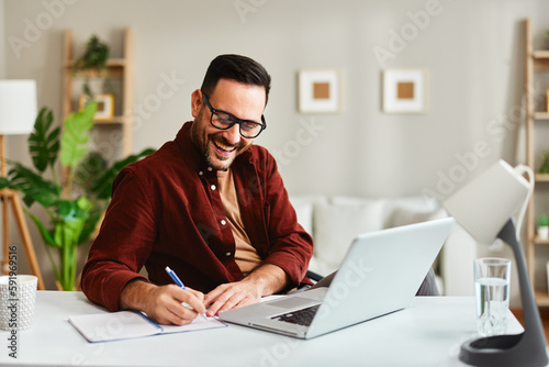 Young business man working at home with laptop and papers on desk.