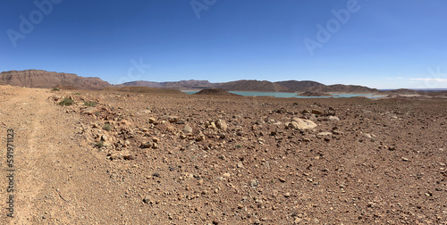 Morocco, Africa: panoramic dirt road and with on the background the view of Barrage Al-Hassan Addakhil, a light blue lake in the valley of the Ziz, in the High Atlas Mountains region 
