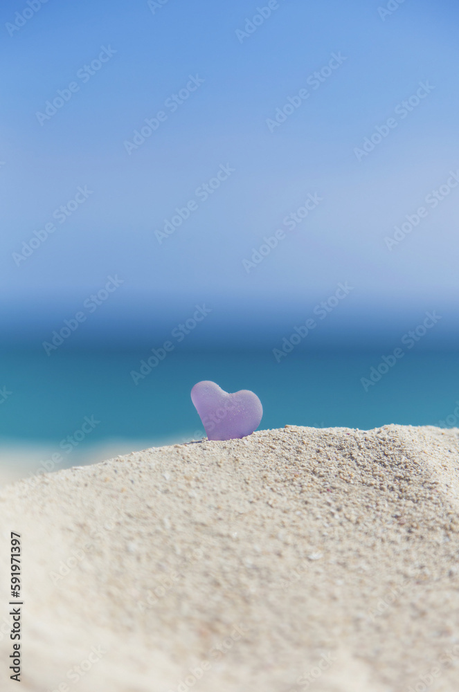 A Lavender Heart Shaped Sea Glass In The Sand At The Beach; Honolulu, Oahu, Hawaii, United States Of America A Lavender Heart Shaped Sea Glass In The Sand At The Beach; Honolulu, Oahu, Hawaii, United States Of America
