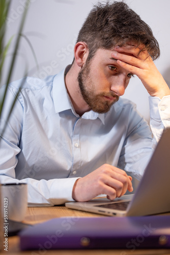portrait d'un étudiant ou d'un employé de bureau fatigué et surmené assis devant son ordinateur portable. Il se tient la tête dans les mains. photo