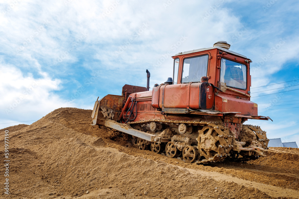 An old orange bulldozer performs work to level the sandy soil An old orange bulldozer performs work to level the sandy soil