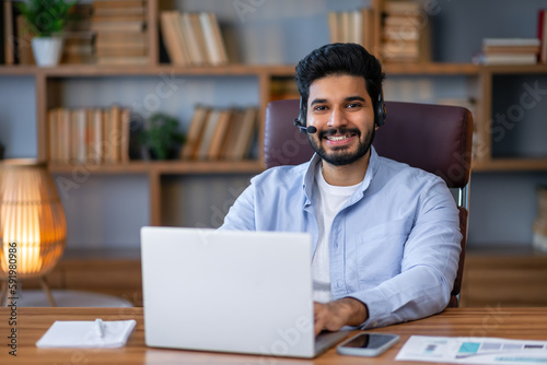 Portrait of smiling millennial Arabic man sit at desk in office have video call with customer or client, happy young Arabian male employee talk on webcam, speak on online webinar