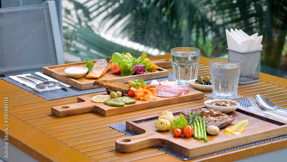 Outdoor restaurant table displays variety of meat cuisine, including grilled beefsteak, smoked salmon, and vegetable omelets. A gourmet meal for any summer holiday. Outdoor restaurant table displays variety of meat cuisine, including grilled beefsteak, smoked salmon, and vegetable omelets. A gourmet meal for any summer holiday.