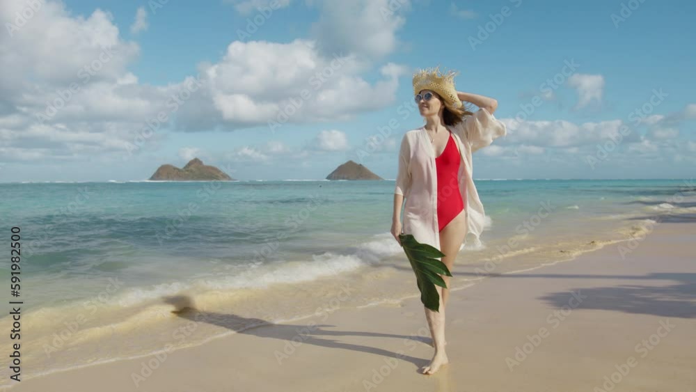 Vacation woman on paradise Lanikai beach on holidays on Oahu island. Girl in straw hat with huge green leaf on luxury travel in resort hotel 4K. Traveller influencer visiting famous Hawaii destination Vacation woman on paradise Lanikai beach on holidays on Oahu island. Girl in straw hat with huge green leaf on luxury travel in resort hotel 4K. Traveller influencer visiting famous Hawaii destination