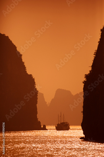 Karst formations and traditional Vietnamese sailboat (thung chai) at sunset in Bai Tu Long Bay in Halong Bay which is a UNESCO World Heritage Site; Halong Bay, Quang Ninh, Vietnam photo