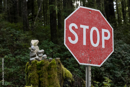 Close-up of a stop sign beside a forested area with moss and a cairn in the background in the community of Bamfield on Vancouver Island; Bamfield, British Columbia, Canada photo