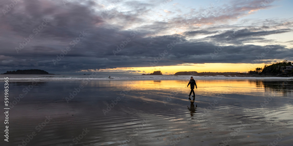A woman walks on the wet beach at low tide and sunset, Chesterman Beach, a renowned surf spot in Pacific Rim National Park Reserve on Vancouver Island; British Columbia, Canada A woman walks on the wet beach at low tide and sunset, Chesterman Beach, a renowned surf spot in Pacific Rim National Park Reserve on Vancouver Island; British Columbia, Canada