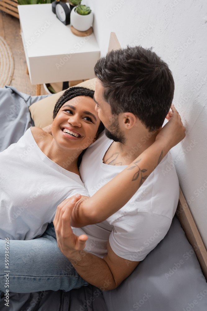 carefree african american woman in white t-shirt embracing boyfriend sitting on bed at home. carefree african american woman in white t-shirt embracing boyfriend sitting on bed at home.