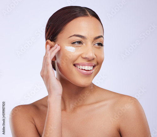 Woman, skincare cream and smile in studio for self care, thinking or beauty with product application on face. Girl, model and facial skin wellness with cosmetics, health and dermatology by background