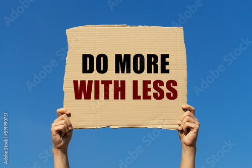 Do more with less text on box paper held by 2 hands with isolated blue sky background. This message board can be used as business concept about doing more with less.